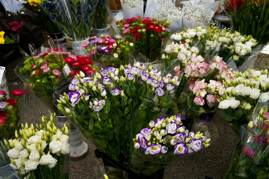 A diverse array of fresh flower bouquets arranged on a countertop, featuring predominantly white, purple, pink, red, and green hues. The bouquets include lisianthus, carnations, and other blooms, each